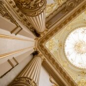 Upward view of a grand interior featuring ornate columns and an intricately designed domed ceiling.