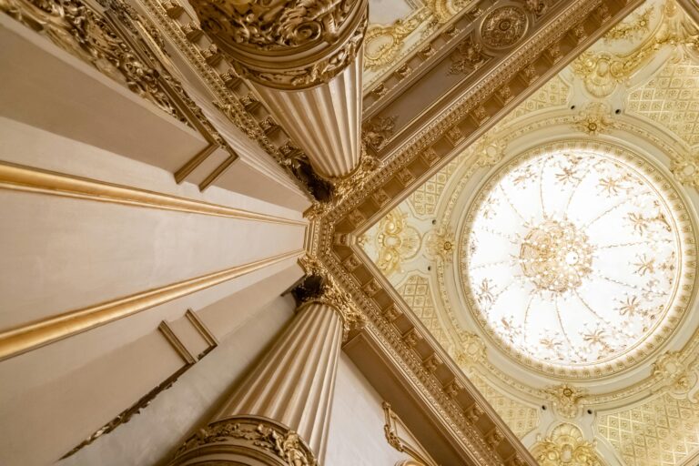Upward view of a grand interior featuring ornate columns and an intricately designed domed ceiling.